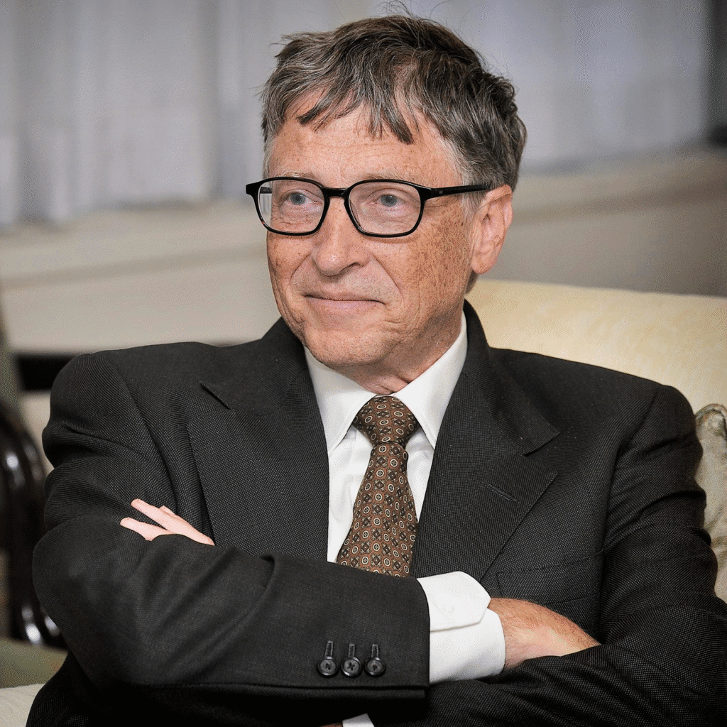 Bill Gates sorrindo em um evento de 2013, usando terno e óculos, com fundo desfocado